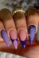 Nails with a gradient design transitioning from purple to pink, with a gold accent on a blurred background, Obroi.