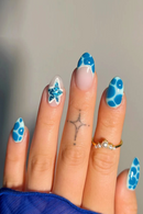 Close-up of a hand with blue nail art on a neutral background, Obroi