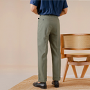 Person wearing green pants and a blue shirt standing in front of a wooden chair, Obroi