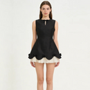 A model wearing a sleeveless black peplum-style top with a keyhole cutout and bow at the collar, paired with a short cream tulle skirt, against a plain off-white studio background, Obroi