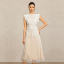 A woman models a sleeveless white and cream tulle midi dress with intricate floral lace applique on the bodice and a sheer tulle skirt, set against a textured beige studio background, Obroi