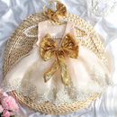 A baby girl's formal party dress in pale blush pink tulle with a large gold sequined bow on the front, displayed on a woven straw mat with a matching headband and pearl necklace, Obroi