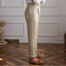 Person wearing beige pants and a white shirt in a room with wooden flooring and white walls, Obroi