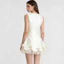 A woman shown from the back wearing a sleeveless ivory dress with a structured back, scalloped hem, and layered tulle skirt with decorative fabric flowers, against a plain light background, Obroi