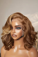 A medium brown wig with blonde highlights and a lace front, displayed on a mannequin head with a hand adjusting the hair on the right side, Obroi