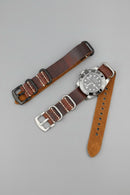 Brown leather watch strap with silver buckle on a dark gray background, Obroi