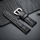 Black leather watch strap with silver buckle on a textured surface, Obroi