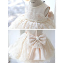 A cream-colored sleeveless flower girl dress displayed on a mannequin, featuring a lace bodice with a pearl bead trim, a tiered tulle skirt, and a large satin bow on the back, Obroi