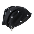 A black slouchy beanie hat decorated with multiple silver rhinestone studs and featuring a silver metal grommet at the bottom, shown on a plain white background, Obroi