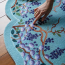 Hand touching a floral patterned rug on a wooden floor, Obroi