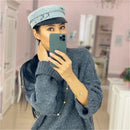 Woman taking a mirror selfie wearing a gray outfit and cap in a room with pink walls, Obroi