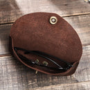 Brown leather case with a gold button holding a pair of glasses on a wooden surface, Obroi