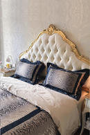 Decorative bed with gold headboard and patterned bedding against a textured wall, Obroi