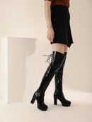 Person wearing black knee-high boots with high heels on a plain background, Obroi