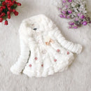 White baby coat with floral embellishments on a white surface with flowers in the background