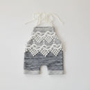 Two baby romper shorts in heathered gray fabric, laid flat on a white background. One has a white textured pocket with two wooden buttons and white drawstrings, and the other has a white lace panel and white drawstrings, Obroi