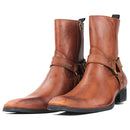 A pair of medium brown leather ankle boots with a western-inspired design, featuring a pointed toe, a decorative strap with a buckle across the instep, and a side zipper, Obroi