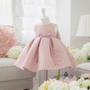 A pink lace toddler girl's party dress displayed on a white mannequin dress form in a bright, softly styled room with floral decorations, Obroi