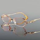Pair of gold-rimmed eyeglasses on a reflective surface with a gray background, Obroi