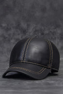 Black leather baseball cap on a textured gray background, Obroi