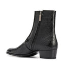 A single black ankle boot with a crocodile-embossed texture, a low block heel, and a side zipper with a silver pull tab, shown from a side profile on a white background, Obroi