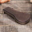 Brown leather pouch with gold zipper on a wooden surface, Obroi