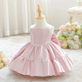 A light pink sleeveless dress with a tiered ruffled skirt displayed on a cream dress form mannequin. The background is a soft, bright room with white curtains and a bouquet of pink and white flowers, Obroi