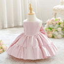 A light pink sleeveless dress with a tiered ruffled skirt displayed on a cream dress form mannequin. The background is a soft, bright room with white curtains and a bouquet of pink and white flowers, Obroi