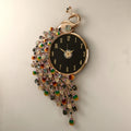 A decorative wall clock with a peacock-inspired design, featuring a black round clock face, gold-tone frame, and dangling multicolored jewel-like embellishments on a light wall. Chinese text at the bottom provides dimensions and weight details, Obroi