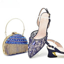 Navy blue high-heeled shoes with crystal embellishments and a matching handbag on a white background, Obroi