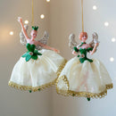 Two angel figurines with green and white dresses hanging against a soft background, Obroi