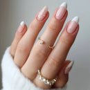 Close-up of a hand with pink and white nail polish wearing gold rings on a neutral background, Obroi