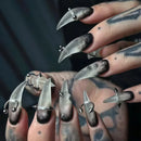 Close-up of a hand with long, pointed nails and metallic accents against a dark background, Obroi