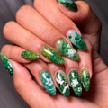 Hand with green floral nail art on a neutral background, Obroi