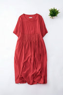 A red short-sleeve dress with a pleated waist, laid flat on a white background with a small green plant in the top right corner, Obroi