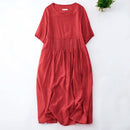 A red short-sleeve dress with a pleated waist, laid flat on a white background with a small green plant in the top right corner, Obroi