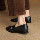 Black loafers worn with brown pants on a beige carpet, Obroi