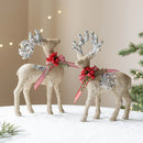 Two glittery deer figurines with red ribbons and silver antlers on a snowy surface, Obroi