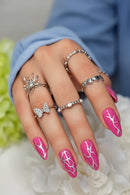Hand with pink nail art and multiple rings against a blurred natural background, Obroi