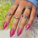 Hand with pink nail art and multiple rings against a blurred natural background, Obroi