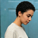 Woman with short black hair wearing a gray shirt against a blue background, Obroi