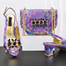 A matching women's accessory set from Obroi, featuring a purple iridescent snakeskin-pattern handbag with gold chain straps and a large black crystal embellishment, alongside two matching high-heeled slingback sandals with gold insoles and crystal-embellished uppers, Obroi