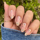 Hand with floral nail design against a blurred green background, Obroi