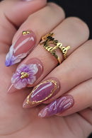 Nail art with floral design and gold accents on a hand wearing a gold ring, Obroi