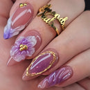 Nail art with floral design and gold accents on a hand wearing a gold ring, Obroi