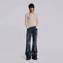 Person wearing a beige long-sleeve shirt and blue jeans on a plain background, Obroi