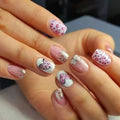 Close-up of a hand with pink and white nail art featuring hearts and glitter, Obroi