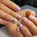 Close-up of a hand with pink and white nail art featuring hearts and glitter, Obroi