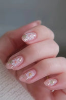 Nails with floral design held by a hand against a neutral background, Obroi