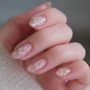 Nails with floral design held by a hand against a neutral background, Obroi